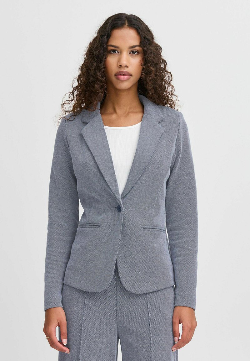 Grå stickad blazer med en notch lapel, enkel knappstängning och två framfickor. Texturerad tyg med en figursydd silhuett.