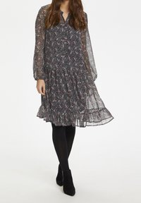Blumendruckkleid mit dunklem Hintergrund, langen transparenten Ärmeln, gerafftem Saum und Knopfleiste am Hals. Getragen mit schwarzen Strumpfhosen und Ankle Boots.