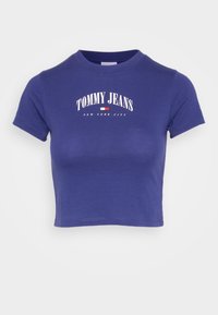 Fioletowy krótki t-shirt wykonany z bawełny, z krótkimi rękawami i okrągłym dekoltem. Wydrukowany tekst zawiera "TOMMY JEANS" oraz "NOWY JORK".