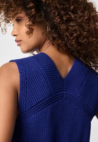 Gebreid mouwloos topje in diepblauw met gestructureerde verticale lijnen en een V-vormige achterkant. Heeft een ribbelachtige halslijn en schouderaccenten.