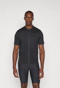 Schwarzes kurzärmliges Fahrradtrikot mit einem Reißverschluss vorne und dezentem Branding auf der Brust, kombiniert mit dunklen, eng anliegenden Fahrradhosen. Glatte Textur.