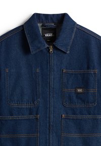 Blauwe spijkerjack met een kraag, een rits aan de voorkant en twee borstzakken. Voorzien van contrasterende gele stiksels en een zwarte Vans-logo patch.