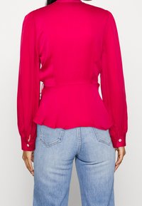 Bledě růžová peplum halenka s dlouhými rukávy a knoflíkovými manžetami, s hladkou texturou a staženým pasem. Nositelná s světle modrými džínami.