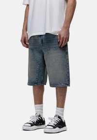 Jasnoniebieskie dżinsowe szorty o luźnym kroju, z dużymi przednimi kieszeniami i prostym wykończeniem, zestawione z czarnymi trampkami i białymi skarpetkami.