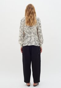 Blusa bianca con motivo astratto nero, maniche a palloncino e polsini elasticizzati. Abbinata a pantaloni cargo neri larghi con tasche laterali.