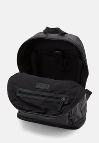 Black backpack with a smooth finish and textured accents. Zippered compartment at the front, multiple pockets inside, and a top handle.