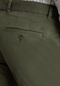 Oliwkowe spodnie w gładkim materiale z tylną kieszenią, z zapięciem na guzik i delikatnym detalem przeszycia.