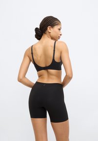 Μαύρο αθλητικό σουτιέν με υφή και ρυθμιζόμενους ιμάντες, σετ με εφαρμοστά μαύρα σορτς, και τα δύο από ελαστικό ύφασμα.