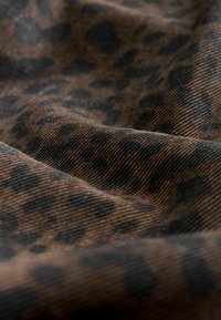 Leopardo rašto audinys su tekstūruota paviršiumi, turintis tamsiai rudos ir juodos spalvos raštus ant rudos fono. Minkšta, audinė medžiaga su subtiliu blizgesiu.