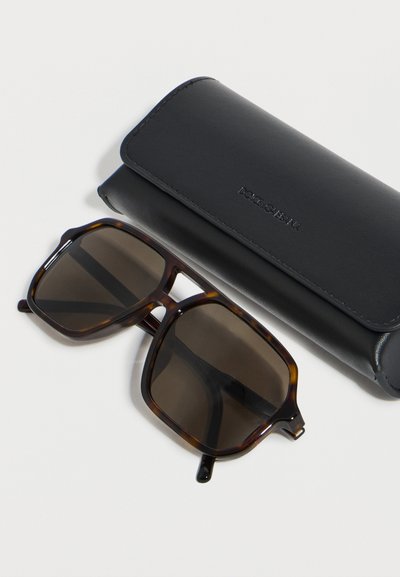 Γυαλιά ηλίου τετράγωνα με σχέδιο χελώνας και σκουρόχρωμους φακούς δίπλα σε μαύρη δερμάτινη θήκη Dolce & Gabbana πάνω σε λευκή επιφάνεια.