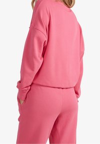 Felpa rosa e pantaloni coordinati in cotone morbido. Vestibilità rilassata, maniche lunghe, polsini a costine e tasche nei pantaloni.