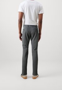 Šedé kalhoty s úzkým střihem a hladkou texturou, s dvěma zadními kapsami a jemnými detaily švů, doplněné bílým tričkem.