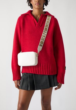 Maglione rosso a maglia con colletto, caratterizzato da polsini a costine. È visibile anche una piccola borsa rettangolare bianca con superficie testurizzata e tracolla grigia.