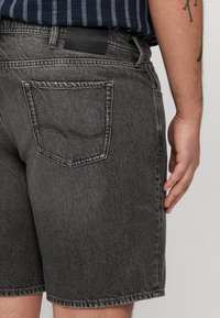 Sive denim kratke hlače s sproščenim fitom, ki vključujejo zadnji žep in vidne šive. Pas ima črno oznako.
