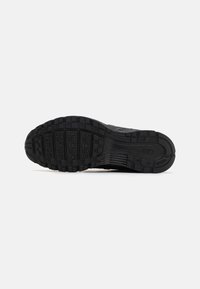Semelle de chaussure de sport noire avec une surface en caoutchouc texturé, comportant des rainures et des motifs pour une meilleure adhérence. Logo Nike embossé près du talon.