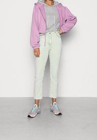 Světle fialová zkrácená mikina přes šedou mikinu, v kombinaci s rovnými džíny mint zelené barvy a multicolorními teniskami.