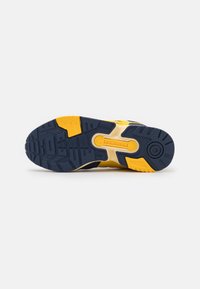 Podeszwa żółto-czarnego buta Adidas pokazująca system wsparcia Torsion oraz teksturowany wzór bieżnika na białym tle.
