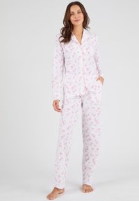 Ensemble de pyjama à manches longues en tissu doux, avec un fond blanc orné de motifs floraux roses. Comprend un haut à boutons et un pantalon.