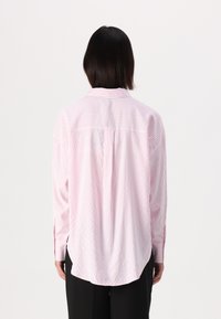 Camicia rosa chiaro con bottoni, a righe verticali bianche, con una piega sul retro e un orlo curvo, realizzata in tessuto liscio. Maniche lunghe.