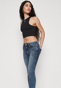 Top corto negro y jeans ajustados de color azul oscuro. Textura acanalada en la parte superior con escote redondo y cierre de botón en los jeans.