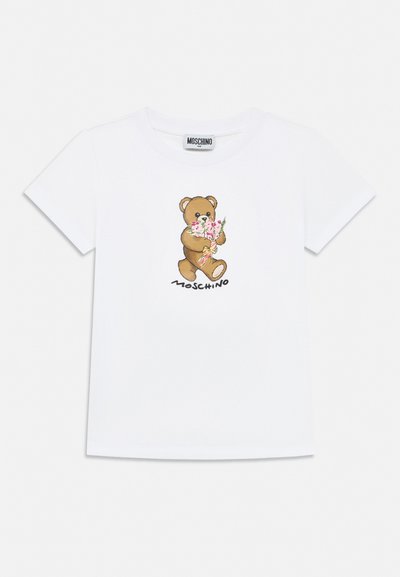 Fehér rövid ujjú póló, amelyen egy maci látható, amint rózsaszín virágokat tart, alatta pedig "Moschino" felirat szerepel elöl.