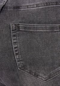 Jeans de mezclilla negra con una vista en primer plano del bolsillo trasero. Las características incluyen una textura sutil, costuras visibles y un diseño clásico del bolsillo.