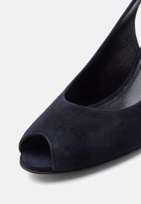 Σύνθλιψη από δέρμα σουέντ σε ναυτικό μπλε με ανοιχτό δάχτυλο και ανατομικό λουράκι στο πίσω μέρος, με χαμηλό τακούνι και εσωτερική επένδυση από δέρμα, απεικονίζεται πάνω σε απλό λευκό φόντο.