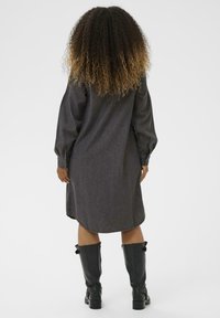 Sötét farmering ruha hosszú, puffos ujjakkal, lekerekített aljjal és gomb részletekkel. Térd fölé érő fekete bőr csizmákkal párosítva.