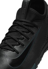 Baskets de sport noires avec un design texturé, des lacets plats et un logo swoosh proéminent dans une teinte plus foncée. Surface lisse et forme ajustée.