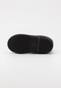 Suela de zapato de goma negra con un pronunciado patrón de onda y círculos, con un borde suave y marca de tamaño en relieve.