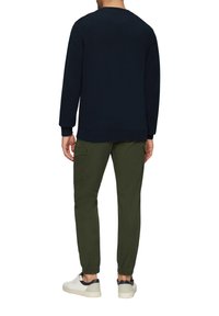 Marineblauer Pullover, gerippte Bündchen, lockere Passform, kombiniert mit olivgrünen, schmal zulaufenden Hosen, elastischen Bündchen und weißen Sneakers mit marineblauen Akzenten.