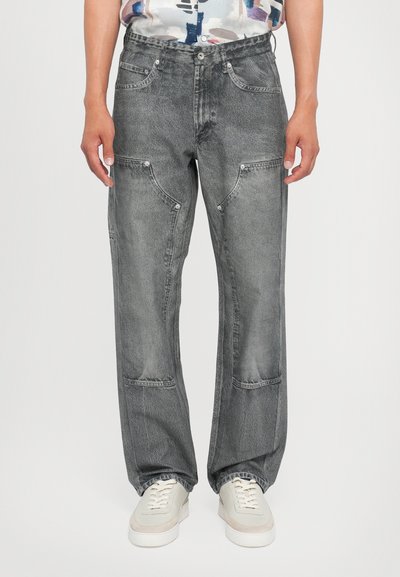 Graue Jeans aus Denim mit einer lockeren Passform, die mehrere Taschen und eine leicht abgenutzte Textur aufweisen. Kombiniert mit weißen Turnschuhen.