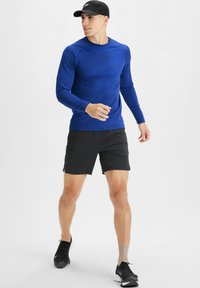 Langärmliges blaues Sportshirt mit Rundhalsausschnitt, kombiniert mit schwarzen Shorts. Das Outfit besteht aus einem glatten, feuchtigkeitsableitenden Stoff.