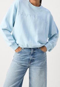 Light blue sweatshirt with crew neck and embroidered "Marc O'Polo" logo, paired with high-waisted light blue jeans. Soft fabric, relaxed fit.