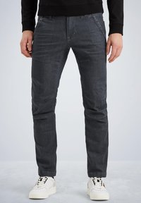 Dunkelgraue Jeans aus Denim mit schlanker Passform, die auffällige Fronttaschen und eine glatte Textur aufweisen, kombiniert mit weißen Sneakers.