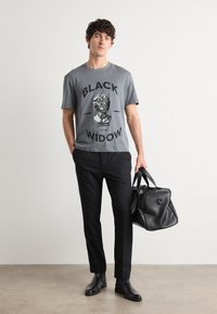 Grå T-shirt med kortärm och svart grafiktryck som säger "BLACK WIDOW", matchad med svarta byxor och en svart gymväska.