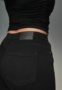 Svarta denimjeans har en figurnära design med hög midja, en mjuk textur och en läderlapp på den bakre midjebandet.