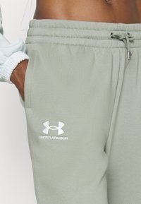 Světle zelené tepláky s elastickým pasem, které mají šnůrku a bílé logo Under Armour na levé kapse. Měkká textilie.