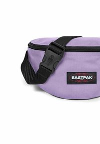 Marsupio in tessuto viola con una tracolla nera regolabile, chiusura con zip e un'etichetta del logo Eastpak sul fronte. Texture liscia.