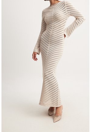Gebreide jurk met lange mouwen en zigzagpatroon in beige met opengewerkte details, nauwsluitend silhouet en een uitlopende zoom. Gecombineerd met lichtgekleurde schoenen.