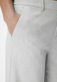 Pantalons taillés gris clair avec une texture lisse, dotés de poches latérales et d'un design à devant plat. Motif de tissu subtil visible.