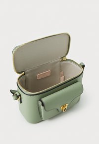 Grønn lærveske med gullglidelås, strukturert design, frontendklaff lukking, og et beige-fôret interiør med et merke-tag.