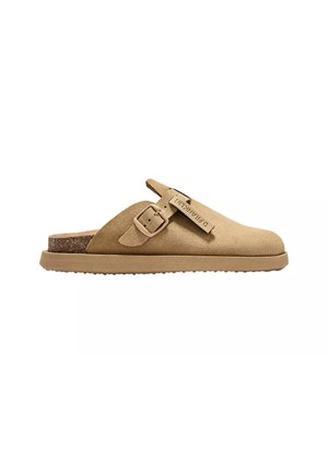 Zoccolo slip-on in camoscio color tan con cinturino regolabile con fibbia e suola in sughero, progettato per un uso casual con etichetta di marca sul cinturino.
