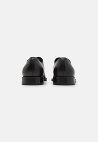 Sorte lærskor med en glatt tekstur, rund form og minimalistisk design. Har en lav, stablet hæl og subtil søm.