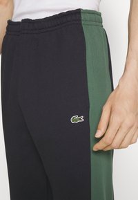 Men's athletic pants with a dark navy and green color block design, featuring an elastic waistband and a small embroidered logo.