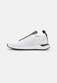 Bílé síťované slip-on tenisky s černými akcenty, texturovaným svrškem, robustním černým poutkem a lehkou gumovou podrážkou s vzorováním.
