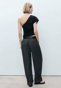Top nero a spalla unica abbinato a pantaloni grigi a vita alta e larghi. Linee pulite, design minimalista e una texture di tessuto morbida.