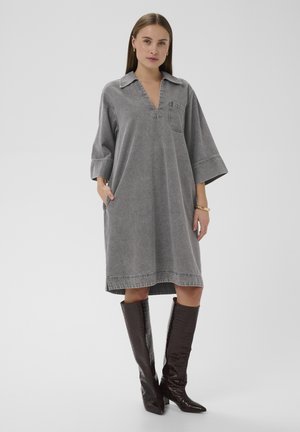 Szara sukienka dżinsowa z dekoltem w serek, krótkimi rękawami, bocznymi kieszeniami oraz kieszenią na piersi. Połączona z brązowymi, sięgającymi kolan, botkami o fakturze imitującej skórę krokodyla.