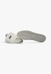 Zapatillas blancas con parte superior de ante, acento trasero azul, cordones planos y suela de goma texturizada con un patrón de espiga.
