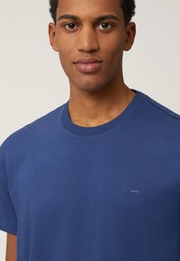 T-shirt in cotone blu a girocollo con maniche corte, caratterizzato da un piccolo logo di un cane ricamato sul petto e una texture liscia e uniforme.